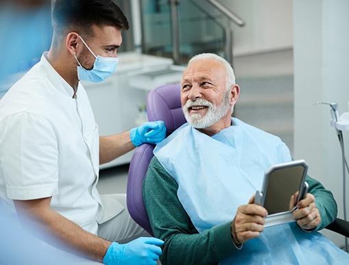 Senior patient looking at dentist while holding small mirror